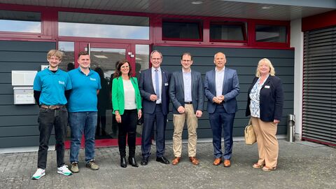 Justizminister Poseck mit der Geschäftsführung und Auszubildenden vor dem Gebäude des Unternehmens.