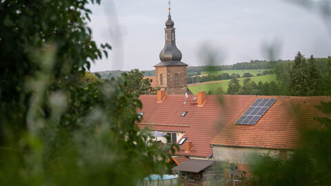 Blick auf Häuserdächer und einen Kirchturm in grüner Landschaft