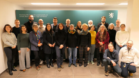 Mehre Personen stehen vor grüner Wand und lächeln in Kamera.