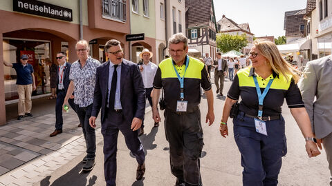 Ministerpräsident Boris Rhein läuft mit zwei Personen in Sicherheitskleidung über die Hessentagsstraße.