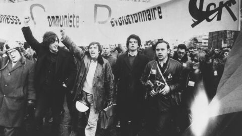 Schwarz-weiß-Aufnahme mit Menschen, die Plakate hochheben und gemeinsam als Gruppe durch die Straße laufen und protestieren.