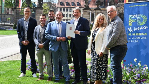 Finanzminister Lorz übergibt den Förderbescheid. Eine Personengruppe steht dabei und schaut in die Kamera.