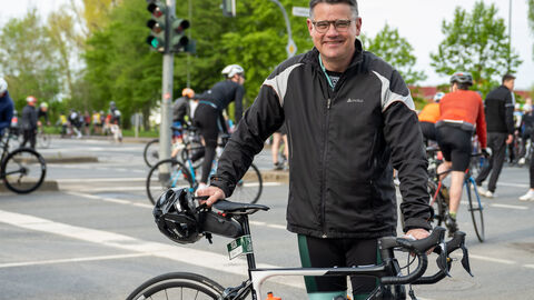Ministerpräsident Rhein steht neben seinem Rennrad und lächelt in die Kamera