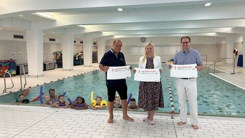 Sportministerin Diana Stolz steht in einem Schwimmbad zwischen zwei Männern. 